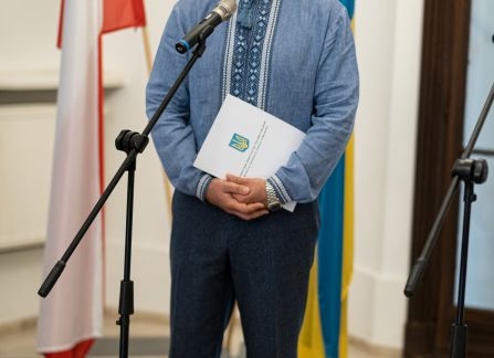 Fotografia. Wernisaż wystawy piękno jedności. Wiaczesław Wojnarowśkyj, Konsul Generalny Ukrainy w Krakowie przemawia do mikrofonu. za nim stoją flagi polska i ukraińska.